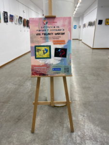 Cartel en un trípode de los VIII Premios UMASAM 2023 y la sala de exposicioens al fondo